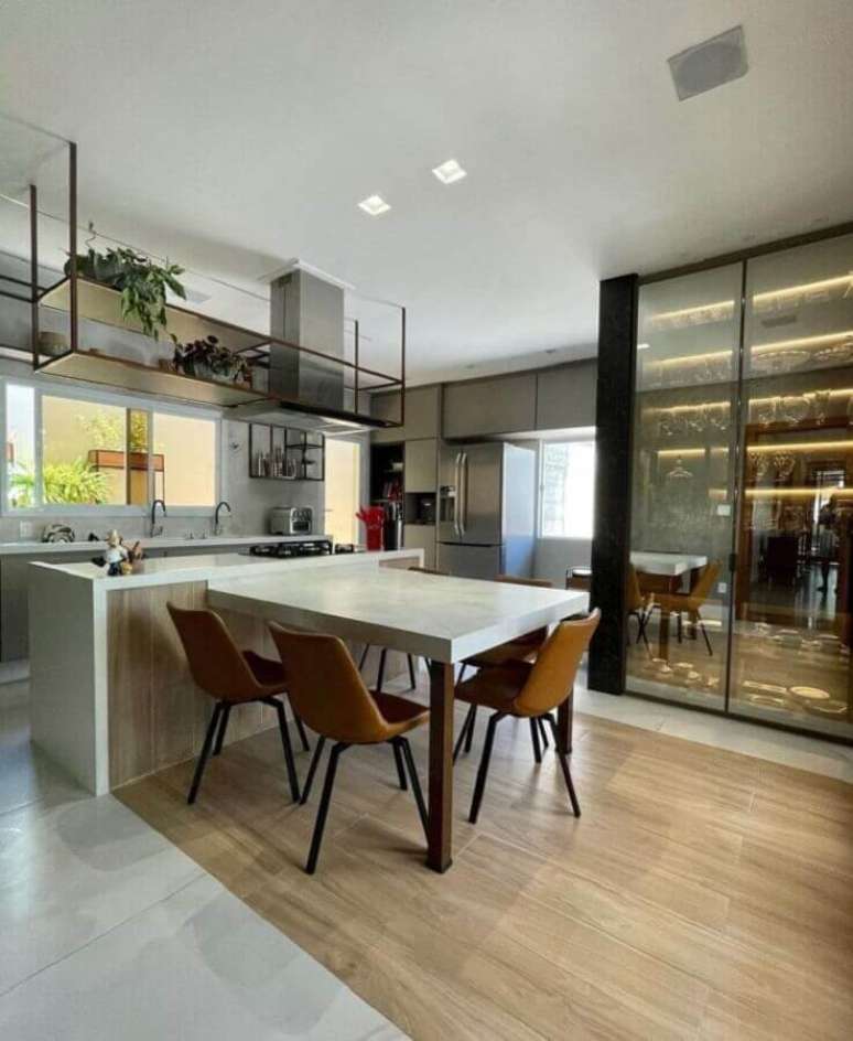 42. Ilha com cooktop e mesa para decoração de cozinha moderna com cristaleira de vidro – Foto: Ludmila Pinto