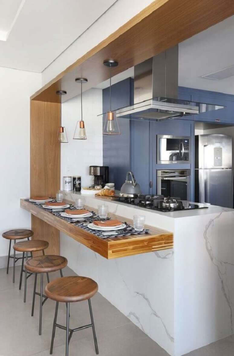 57. Ilha de mármore com cooktop e bancada de madeira para decoração de cozinha azul – Foto: Bianchi e Lima Arquitetura