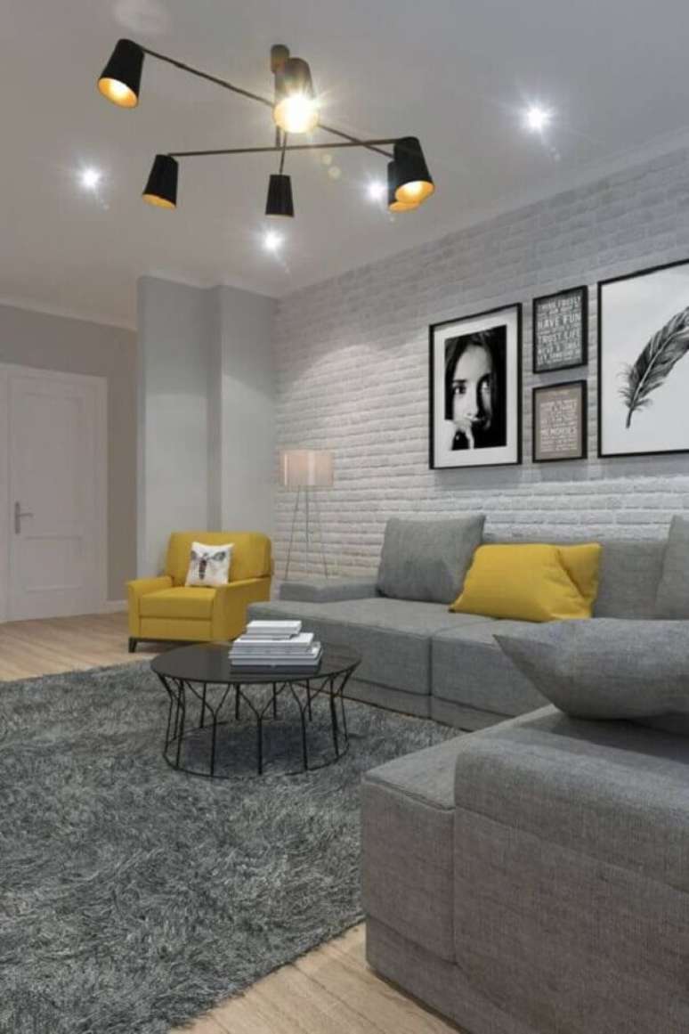 37. Iluminação sala de estar cinza e amarela decorada com parede de tijolinho branco – Foto: Boca do Lobo