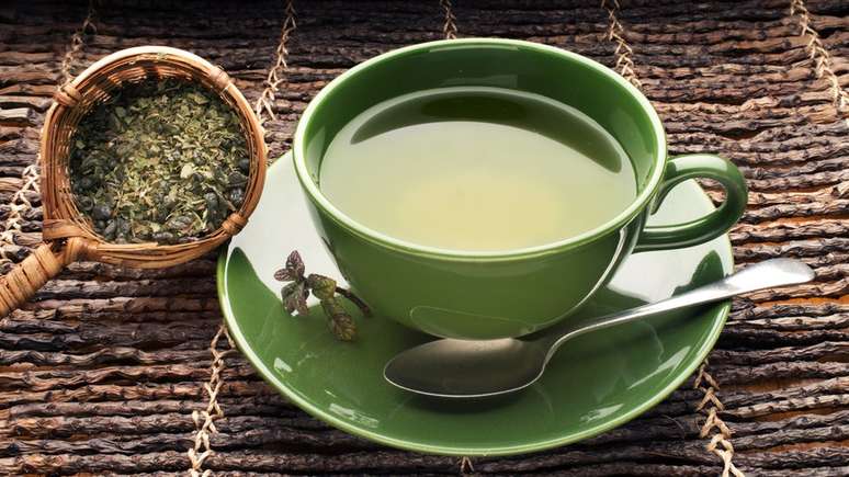 Mesa com chá verde e ervas ao lado