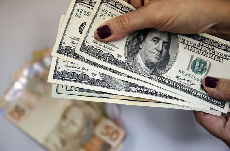 Mulher segura notas de dólar com cédulas de reais ao fundo. Rio de Janeiro, Brasil. 31 de março de 2015. REUTERS/Sergio Moraes