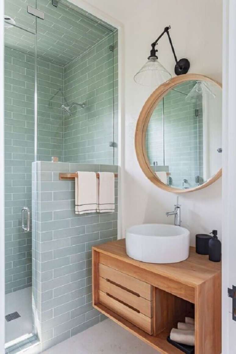 35. Decoração de banheiro verde claro com espelho redondo e gabinete de madeira – Foto: Archidea
