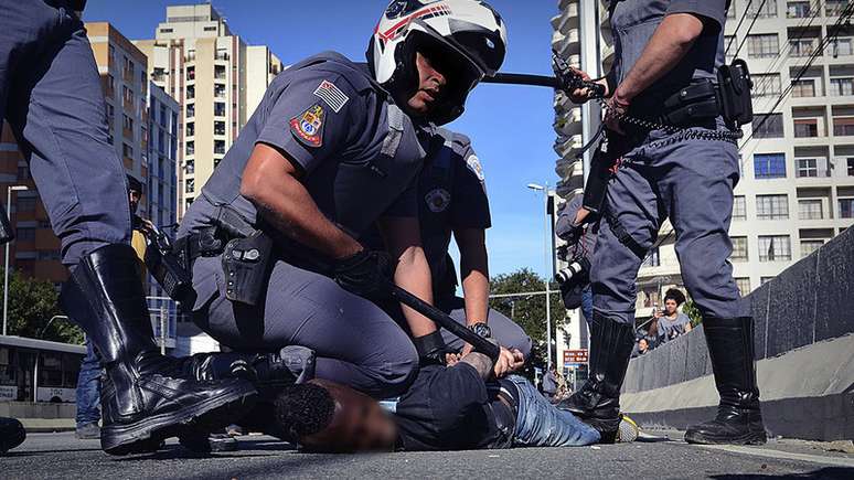 Imagem mostra grupo de policiais militares imobilizando jovem negro no asfalto