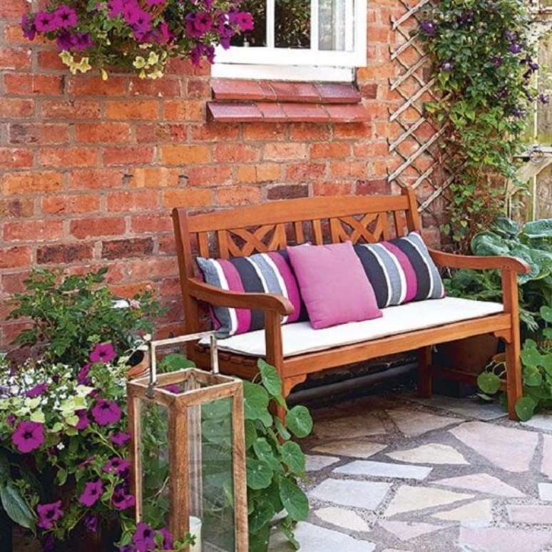 17. Banco de jardim decorado com almofadas roxas e luminária de jardim de chão – Foto Ideal Home