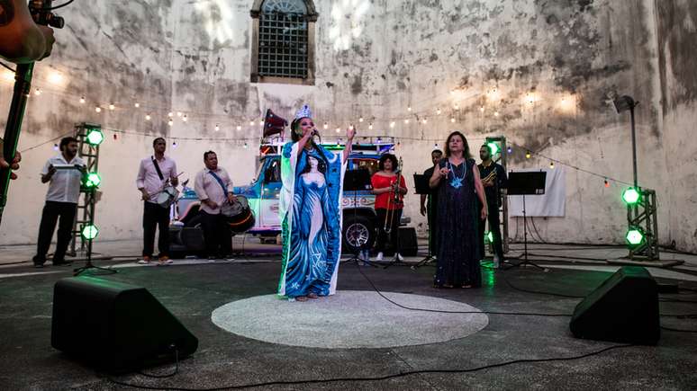 Imagem mostra palco com duas cantoras e um carro de som com luzes coloridas atrás