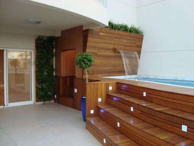 17- A cascata para piscina com led tem a saída de água na parede revestida de madeira. Fonte: Pinterest