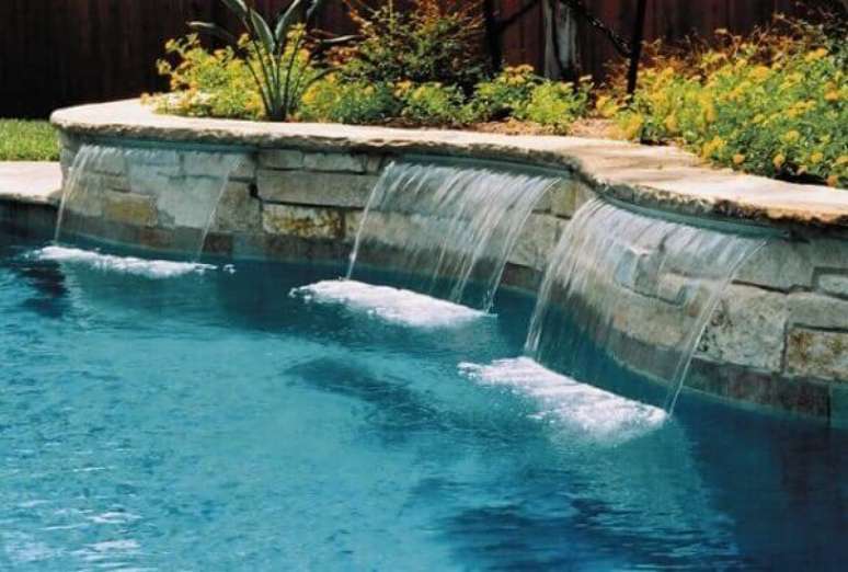 28 – A cascata para piscina tem as saídas de água do canteiro de plantas. Fonte: Piso Para Piscinas
