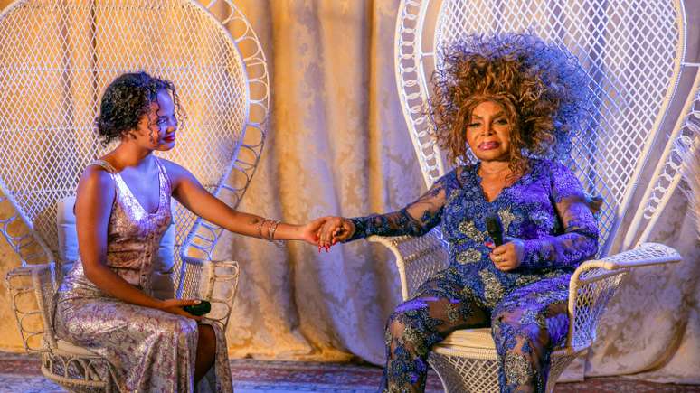 Imagem mostra as cantoras Agnes Nunes e Elza Soares. As duas estão sentadas em poltronas e dão as mãos.