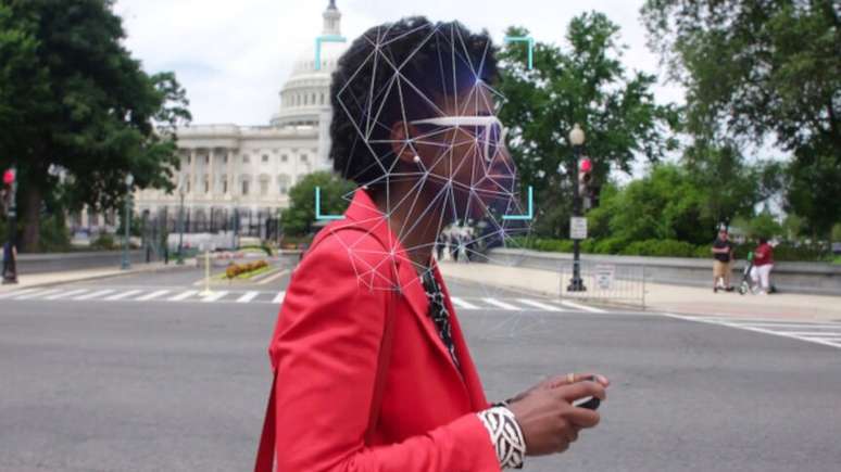 Imagem mostra mulher negra, com terno vermelho, de perfil, caminhando na rua.