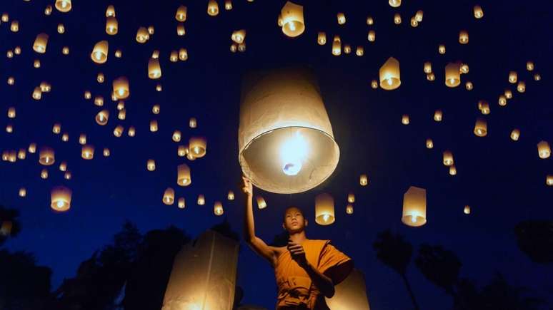 Monge levanta objeto luminoso, em meio a escuro com outros pontos de luz