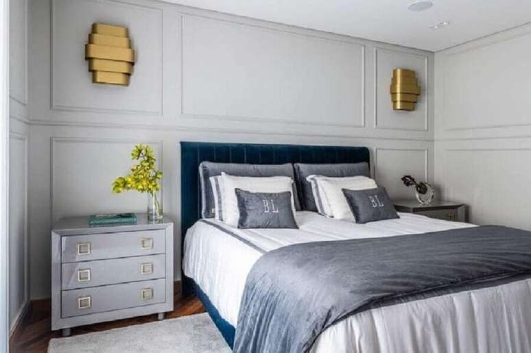 60. Quarto com boiserie decorado em tons de cinza com lumin&aacute;ria de parede dourada &ndash; Foto: Erica Salgueiro