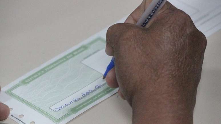 Imagem mostra a mão de uma pessoa negra segurando uma caneta e escrevendo o nome no título de eleitor