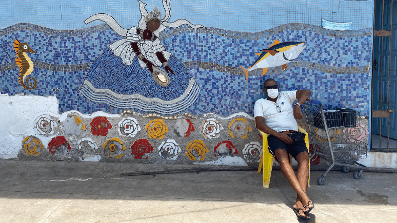 A imagem mostra um pescador com uma imagem de Yemanj&aacute; atr&aacute;s