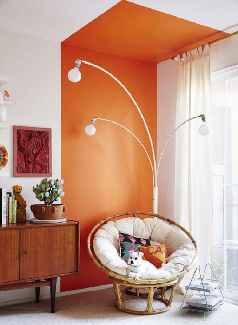 14. Parede de sala decorada com pintura setorizada laranja perto do rack minimalista e poltrona de ratan &ndash; Foto Casa Vogue