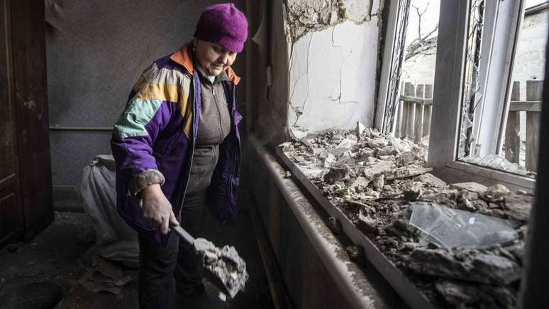 Mulher limpa a casa danificada após ataque de artilharia de uma área de Donetsk, sob o controle de rebeldes apoiados pela Rússia