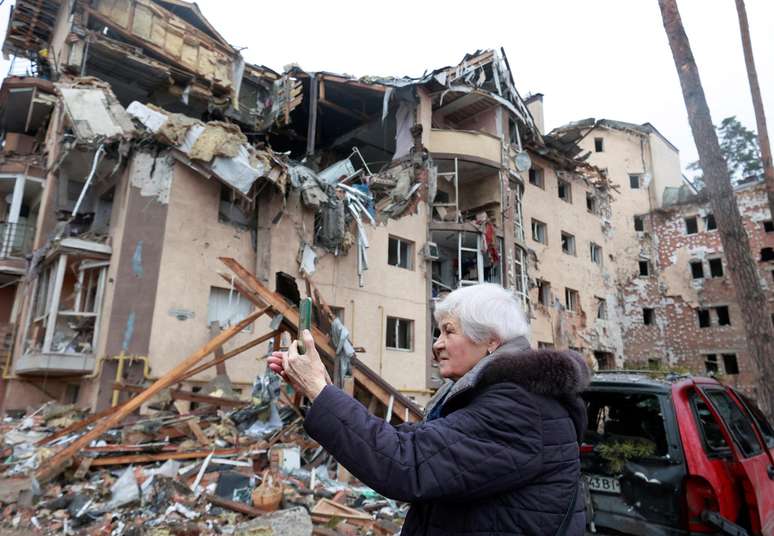 Uma mulher usa um smartphone em frente a um prédiob residencial destruído por bombardeios recentes, enquanto a invasão russa da Ucrânia continua, na cidade de Irpin, na região de Kiev