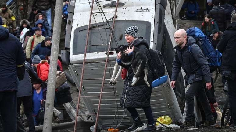 Uma mulher carrega um cachorro enquanto as pessoas atravessam uma ponte destruída na cidade de Irpin, a noroeste de Kiev, em 5 de março de 2022