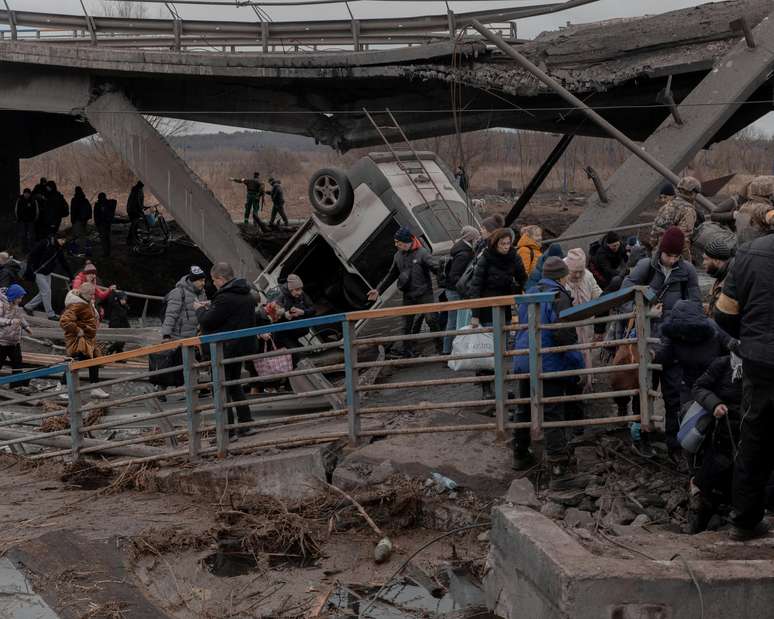 Refugiados atravessam uma ponte destru&iacute;da ao tentar deixar a cidade de Irpin