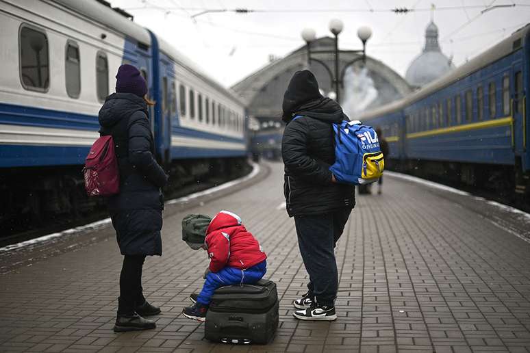 Evacuees and a child, sitting on top of a suitcase, wait for a train to Romania from Lviv