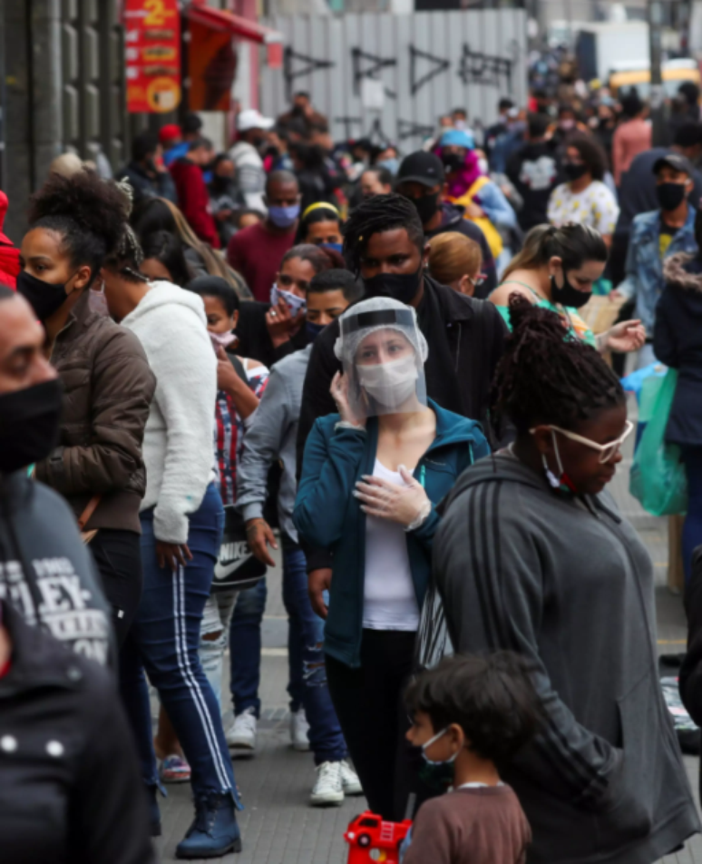 Mulher usando máscara protetora e protetor facial fala ao telefone enquanto pessoas caminham em uma popular rua comercial em meio ao surto de Covid-19 em São Paulo, Brasil, 15 de julho de 2020