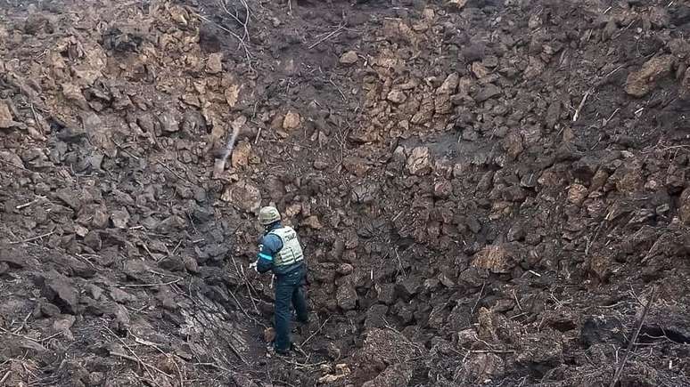 Membro dos serviços de emergência ucranianos examina uma grande cratera de bomba em hospital infantil e maternidade em Mariupol