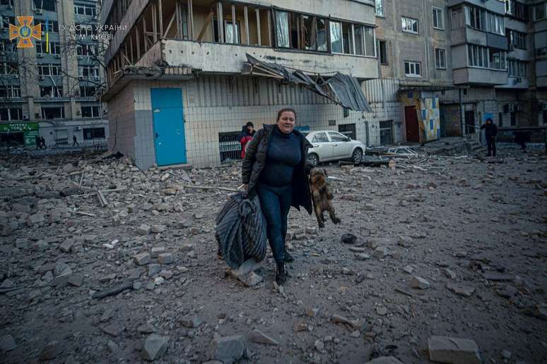 Uma mulher segura o seu cachorro na saída de um prédio residencial atingido ataques russos em Kiev, registrados nesta quarta-feira, 16