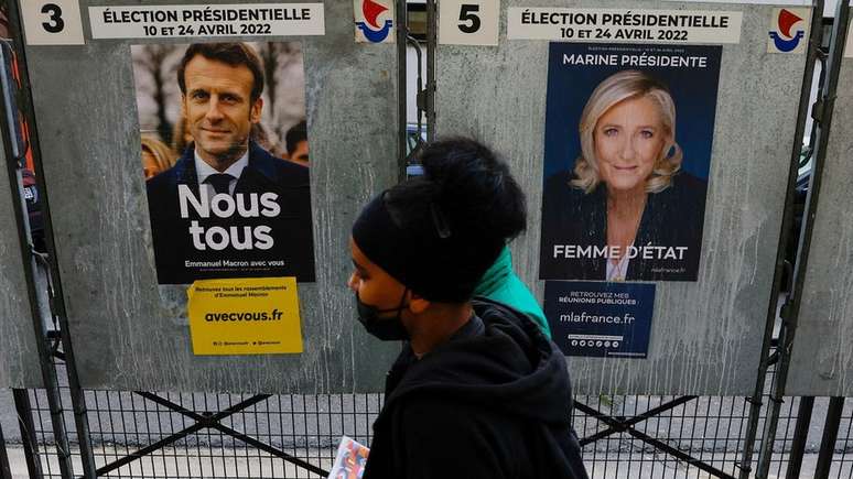 Pessoas caminham diante de cartazes da campanha de Emmanuel Macron e Marine Le Pen
