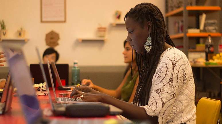 Imagem mostra uma mulher negra em um ambiente corporativo digitando em um notebook.