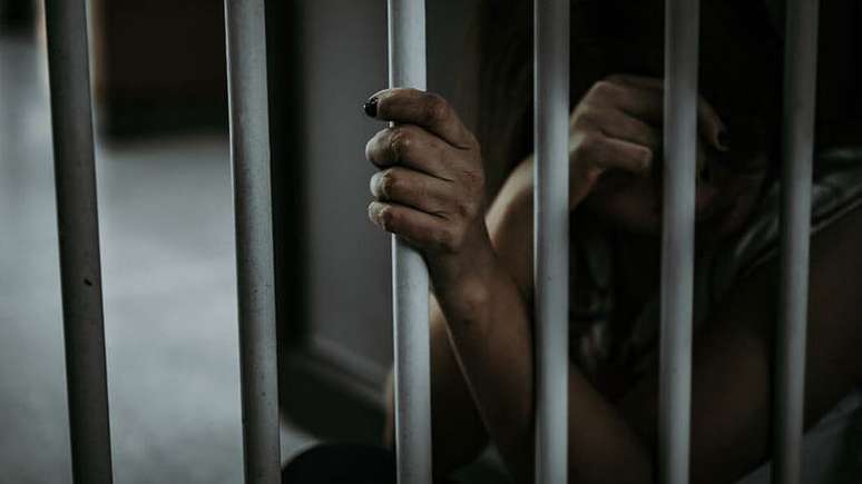 Imagem mostra mão de mulher negra com unhas pintadas de preto segurando grade de cela