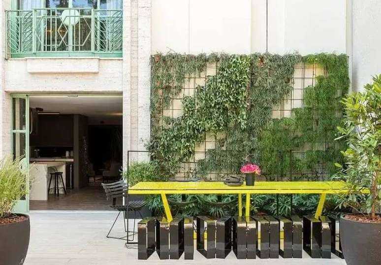 15. Área de lazer com mesa de madeira amarela e jardim vertical externo. Fonte: Studio Clariça Lima