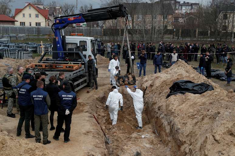 Médicos forenses exumam corpos de civis encontrados em valas na cidade de Bucha, norte de Kiev, no dia 13 de abril. Evidências revelam que mulheres foram estupradas na cidade antes de serem mortas por russos 