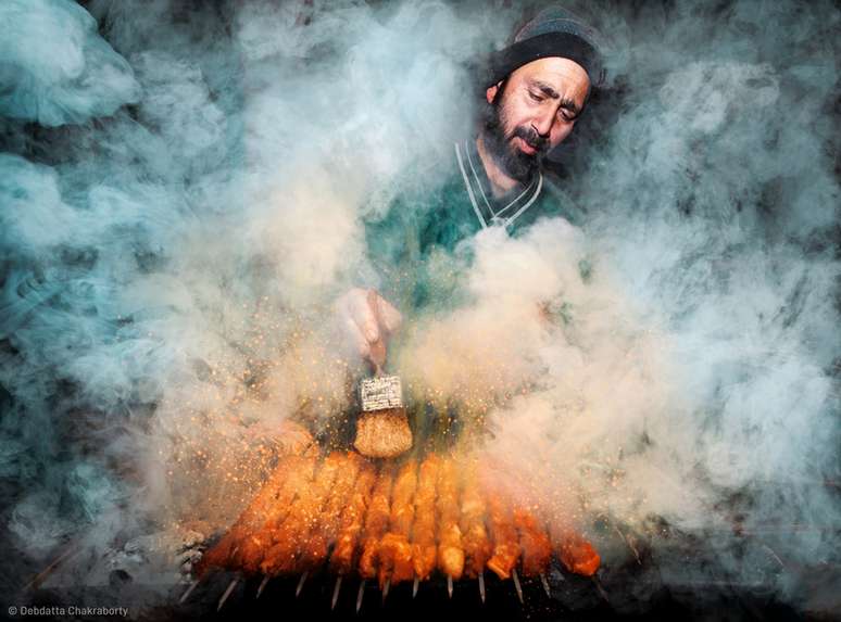 Vendedor de comida de rua cercado por fumaça enquanto prepara comida