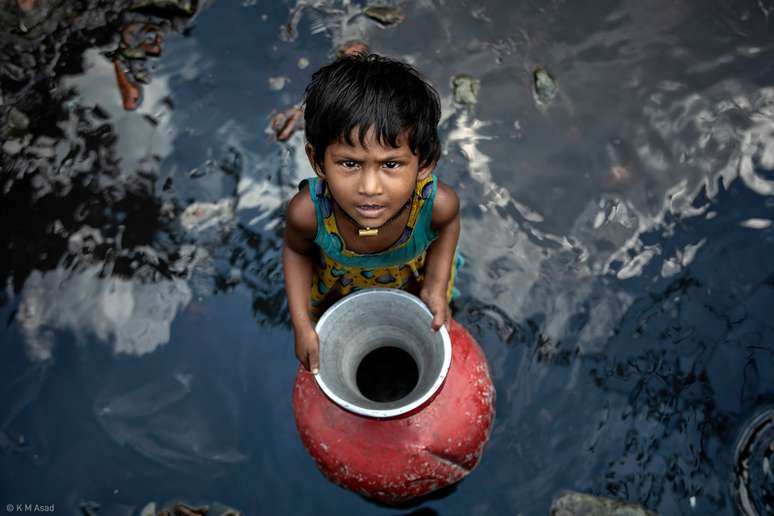 "Uma garotinha coleta água com sua irmã mais velha na favela Chad Uddan em Dhaka, em Bangladesh, em setembro de 2021."