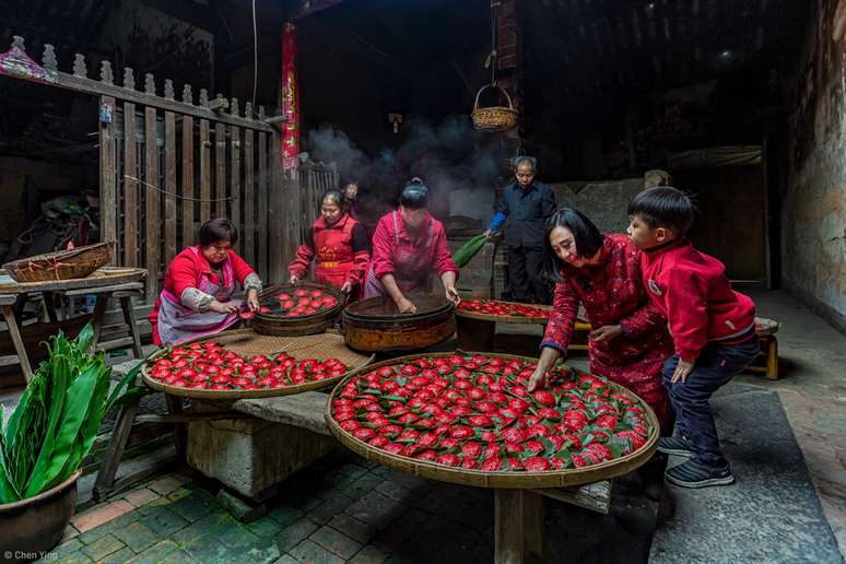 "Foto feita em uma pequena fazenda na vila de Qianlian, condado de Xiangyou, cidade de Putian, província de Fujian. Uma família se reúne para fazer bolinhos recheados de arroz e feijão. Eles usam um selo de madeira para carimbar as palavras 'fortuna' ou 'felicidade' na massa vermelha e cozinham os bolinhos no vapor em uma grande panela. Essa tradição significa que o Ano Novo será recebido com reencontro e o próximo ano será próspero."