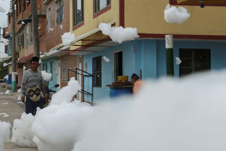 Homens conversam em rua onde há espuma vinda de um rio em Mosquera