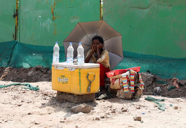 Garota vende água debaixo de guarda-sol em meio ao forte calor em Nova Délhi 27/04/2022