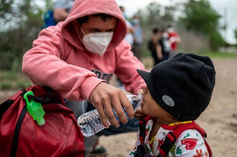 Um imigrante dá água à sua filha perto da fronteira EUA-México em Del Rio, Texas. Foto tirada em 16 de maio de 2021