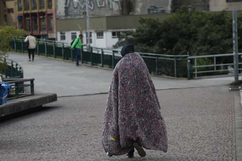 Pedestres e moradores em situação de rua tentam se proteger do frio na Praça da Bandeira em São Paulo 