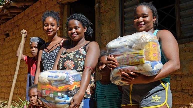 Foto com seis quilombolas, entre mulheres e crianças. Duas mulheres seguram cestas de alimentos.