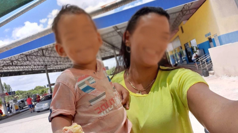 Imagem mostra a mãe, Paula Laís, segurando o menino Samuel no braço. Ambos estão com os rostos embaçados