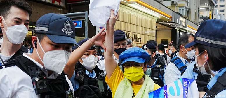 Mulher portando folha de papel em branco é controlada por policiais em Hong Kong 