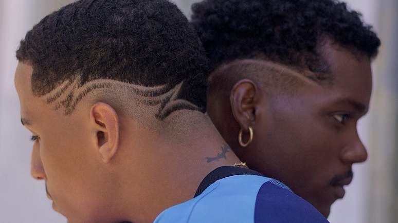 Imagem enquadra dois jovens negros em perfil com desenhos na lateral da cabeça