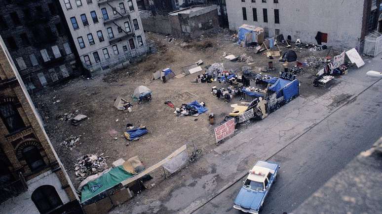 Viatura da pol&iacute;cia observa acampamento de sem-tetos montado em um terreno abandonado no East Village, Nova York, em 1991