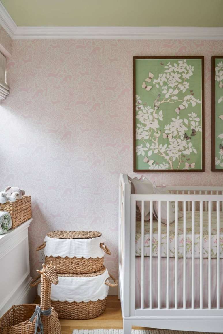 Quarto infantil com berço, papel de parede rosa, e quadro com detalhes verdes.