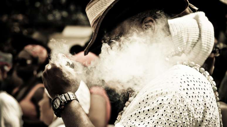 Imagem mostra um homem soltando fumaça de cachimbo.