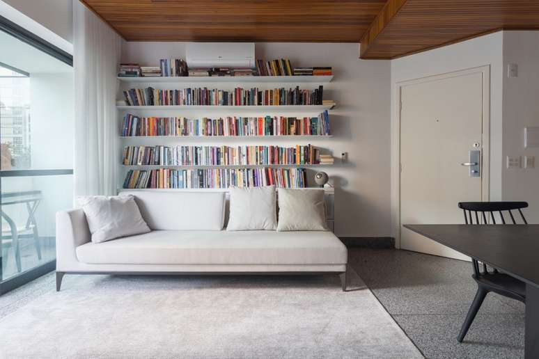 Sofá creme, parede de fundo com diversos livros apoiados em prateleiras.