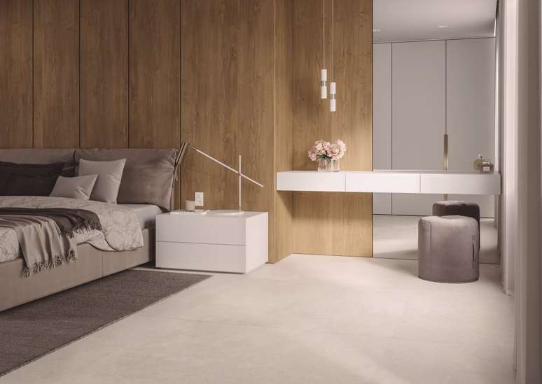 Foto mostra quarto de casal com piso cer&acirc;mico claro, parede revestida com painel de madeira e mobili&aacute;rio em tons de branco e bege.
