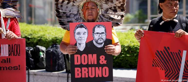 Indígena brasileiro segura cartaz com os rostos do indigenista Bruno Pereira e do jornalista britânico Dom Phillips durante manifestação em Bruxelas