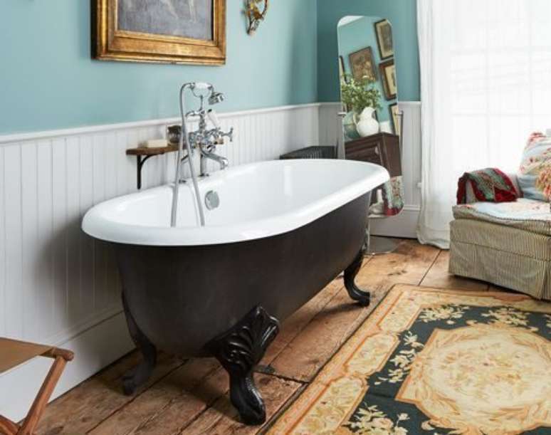 Banheiro com banheira vintage de p&eacute;s de garra, o lado externo &eacute; preto e o interno branco.