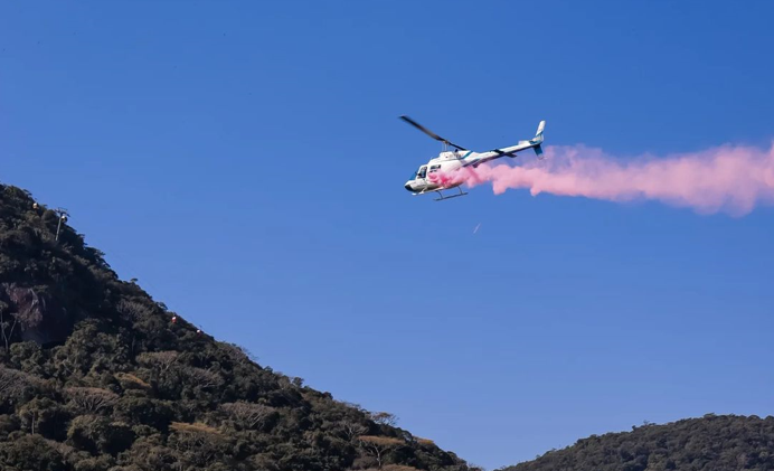 Helicóptero sobrevoando e lançando um pó rosa sobre o mar